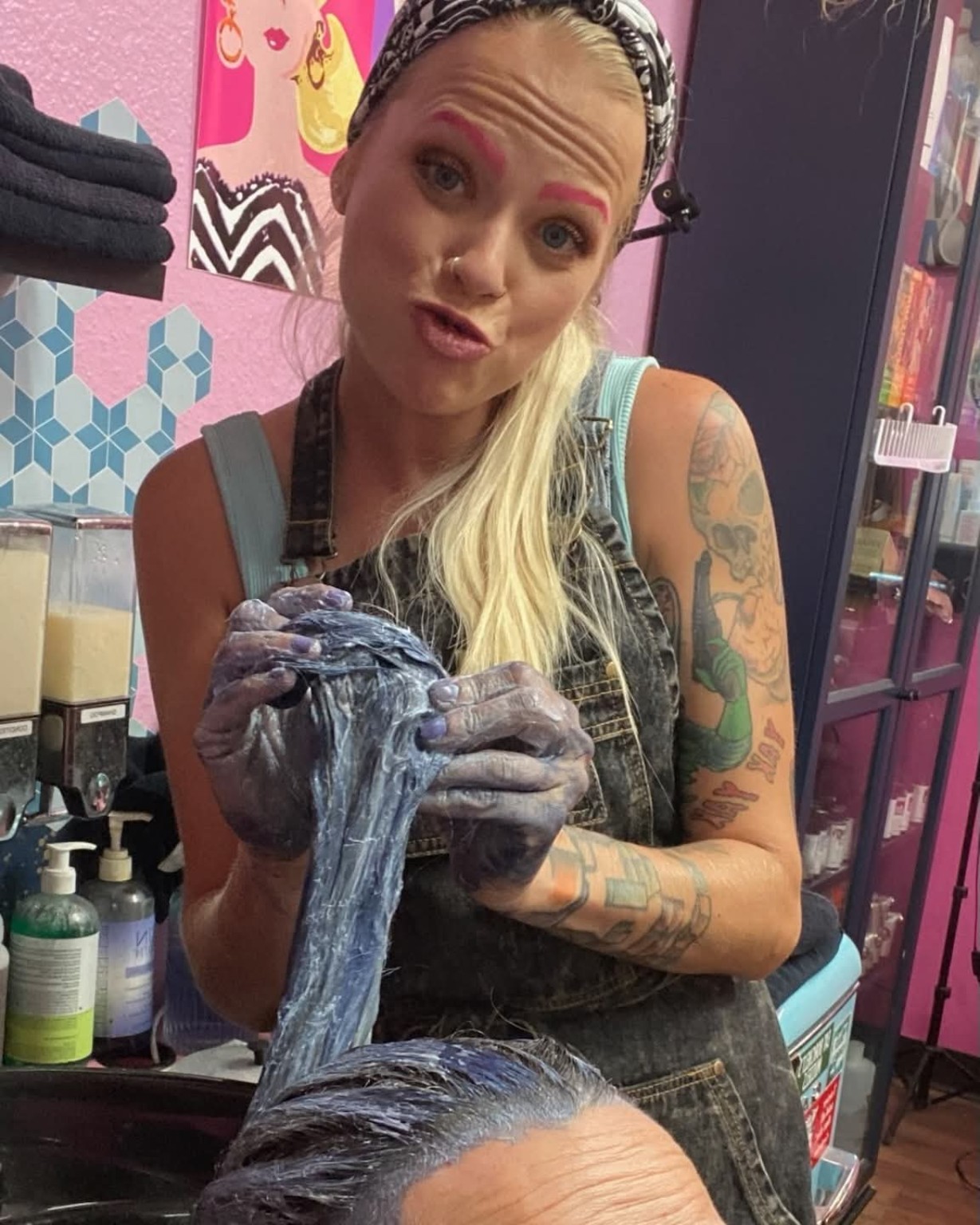 Jenn playfully holding blue-toned hair color while working behind the chair